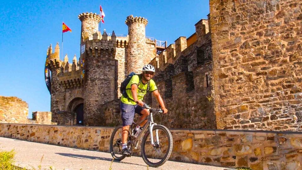 Cyclist on the Camino de Santiago trail passing historic landmarks in Spain.