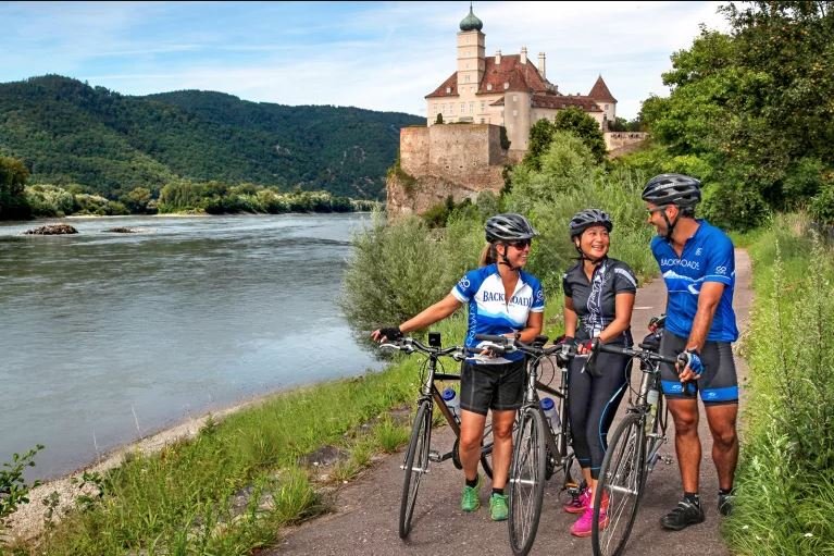 Cyclists riding along the Danube River with scenic views of castles and towns